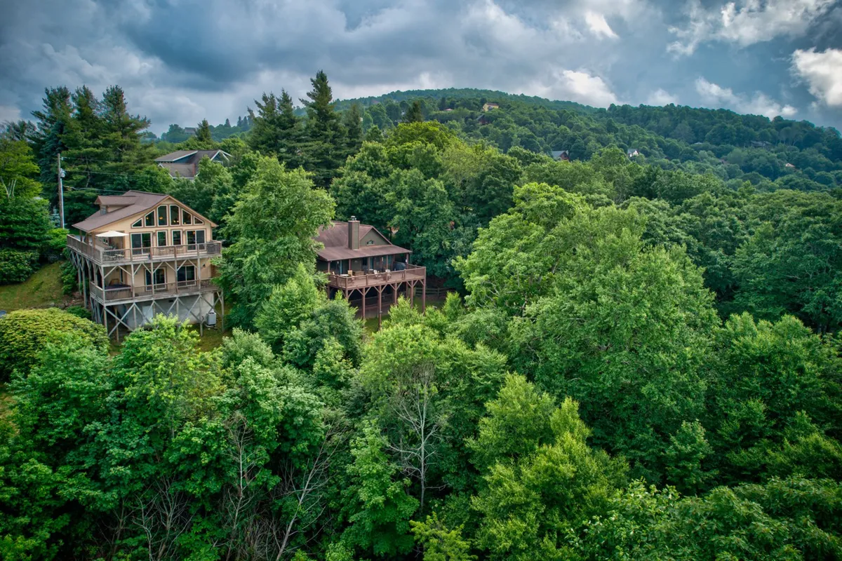 This image features two mountain homes nestled amidst lush trees and rolling hills, emphasizing the privacy, tranquility, and opportunity for group getaways with nearly identical sister homes.