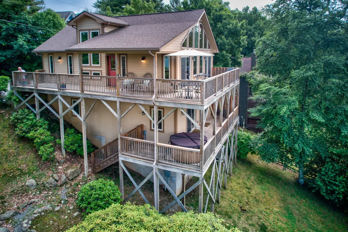 A welcoming elevated wooden deck surrounded by lush greenery, with large windows offering a glimpse into the home's interior. The space features ample room for outdoor dining or family gatherings while enjoying the fresh mountain air.