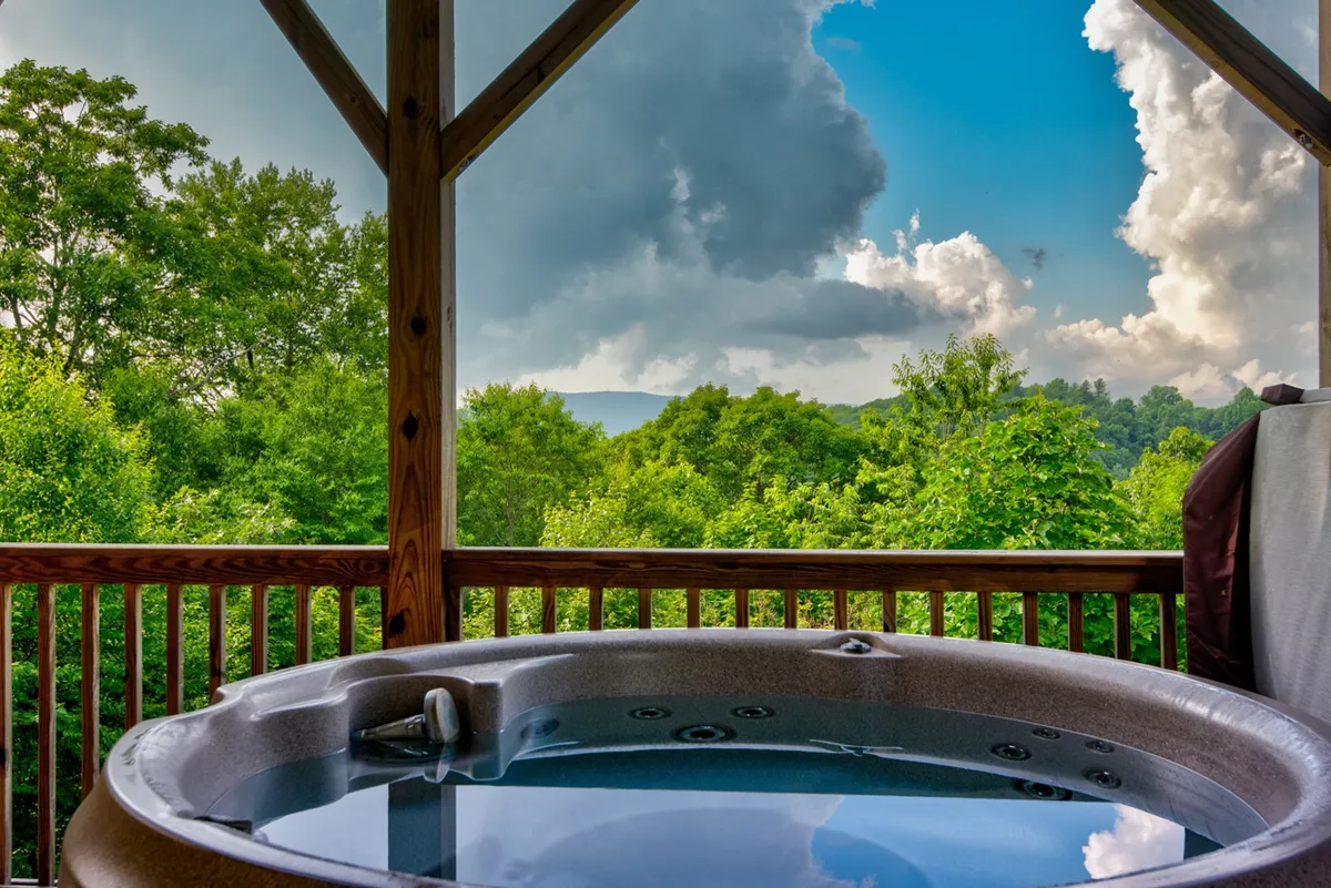 A tranquil exterior scene featuring a hot tub perched to take in sweeping mountain views and surrounded by lush greenery. The setting is ideal for relaxation, sunset watching, or stargazing after a day of fun.
