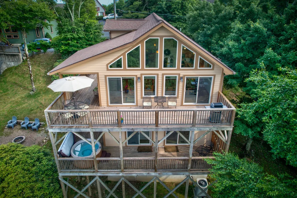 This image showcases the home's exterior deck with a hot tub, ample seating, and large windows that highlight the seamless blend between indoor luxury and outdoor relaxation. The deck is tranquil and inviting, surrounded by nature, making it ideal for unwinding or socializing.