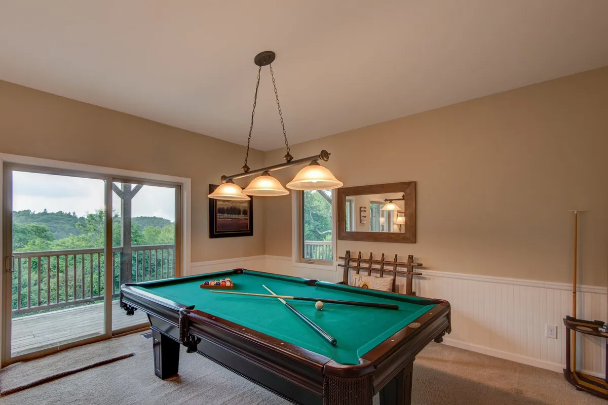This interior image prominently features a pool table set in a room with large windows providing scenic views. Stylish lighting fixtures add a modern touch, and the room exudes a casual, entertaining atmosphere ideal for game nights.