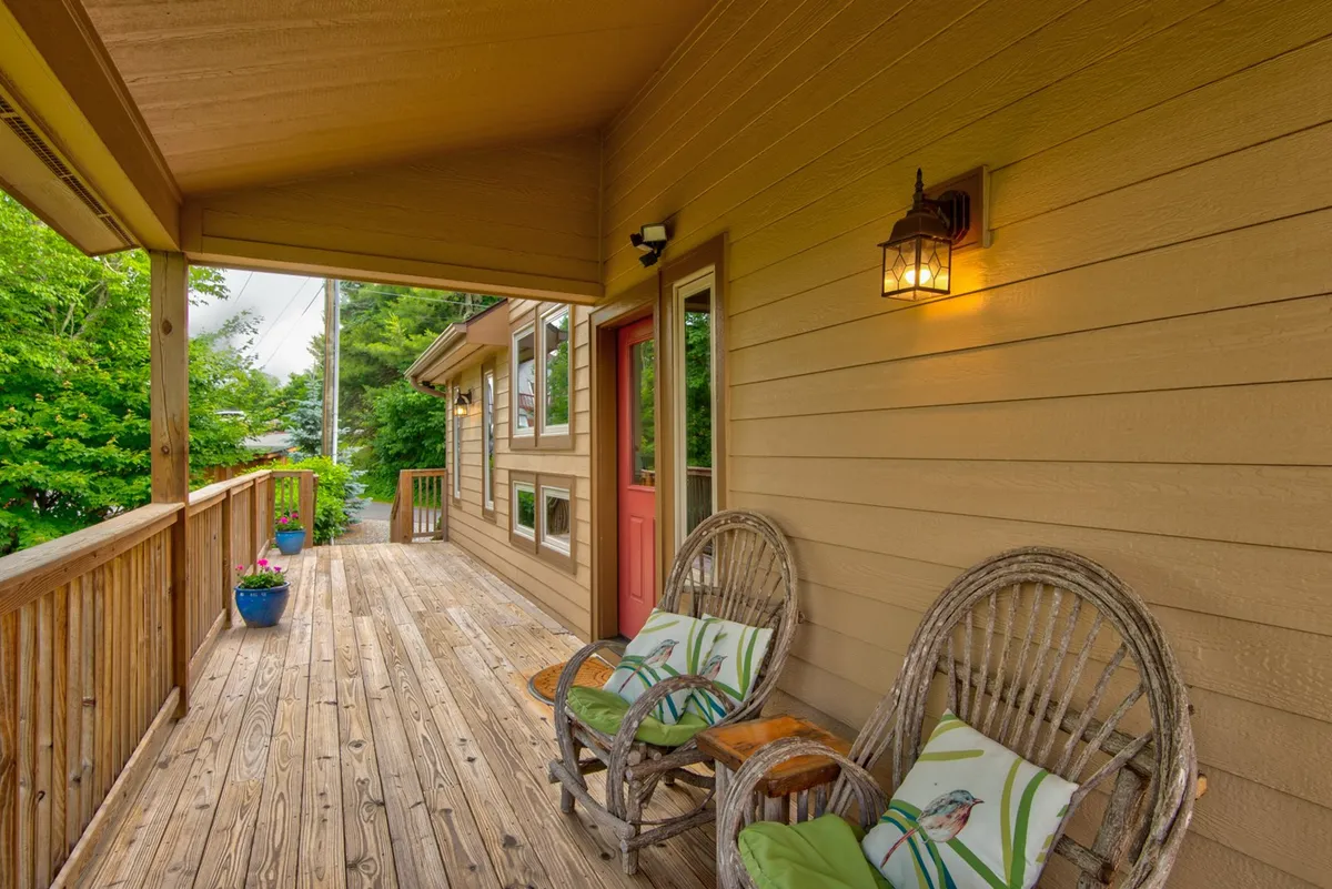 A welcoming view of a wooden deck with rocking chairs, colorful planters, and a red door. The scene exudes hospitality and comfort, while the open deck area hints at a pet-friendly, accessible environment.