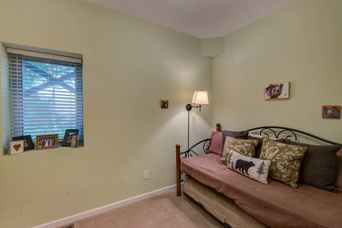 A welcoming sitting room with a daybed adorned with decorative pillows, a window with blinds letting in soft light, and a lamp on the side table. The space feels comfortable and versatile, ideal for both quiet reading and extra sleeping arrangements.