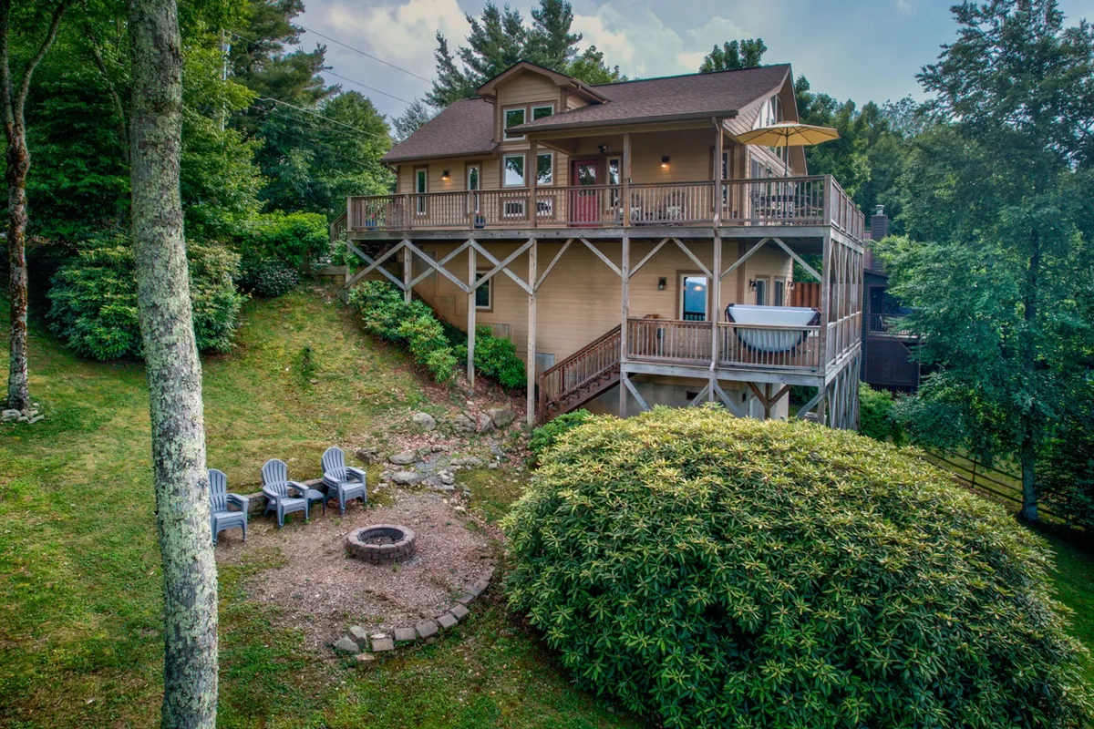 An inviting exterior shot showcases a multi-level deck with a fire pit surrounded by seating and lush greenery. The deck captures the spirit of outdoor gatherings, with areas for relaxing, enjoying views, and making s’mores by the fire.
