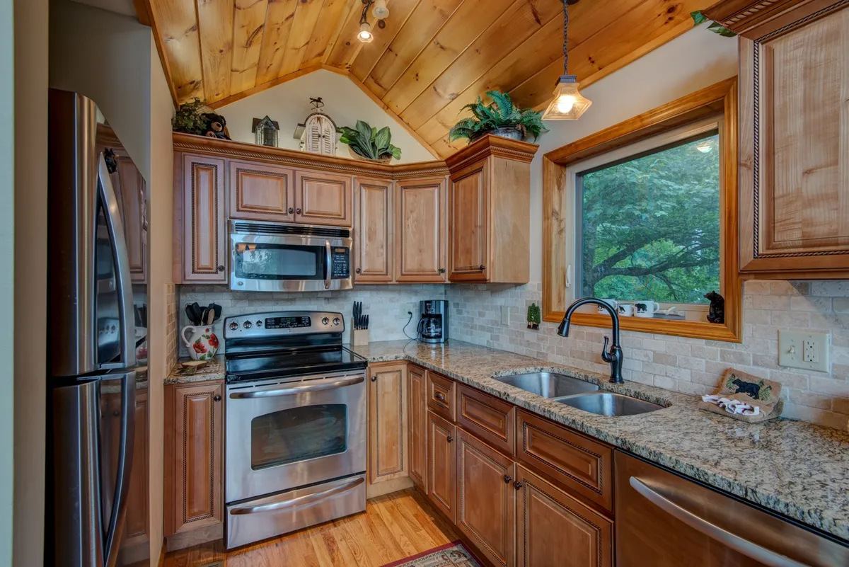 A close-up view of the gourmet kitchen featuring granite countertops, stainless steel appliances, wooden cabinetry, and a large window with a view. The layout is both functional and stylish, ideal for morning coffee or preparing meals with a view.