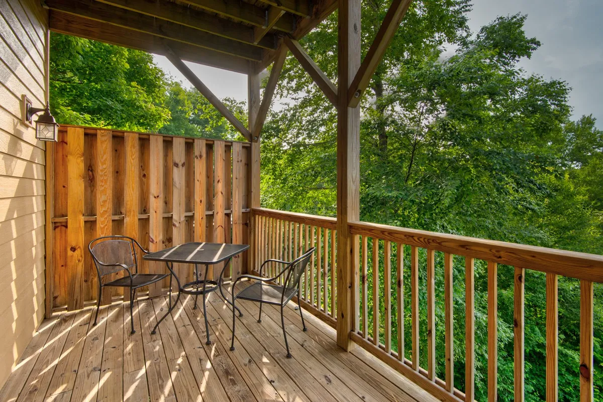 An exterior scene featuring a small black table and two metal chairs nestled among vibrant greenery, ideal for enjoying a quiet morning or evening outdoors with a pet. The setting feels relaxed and intimate, suggesting easy access to outdoor comfort.