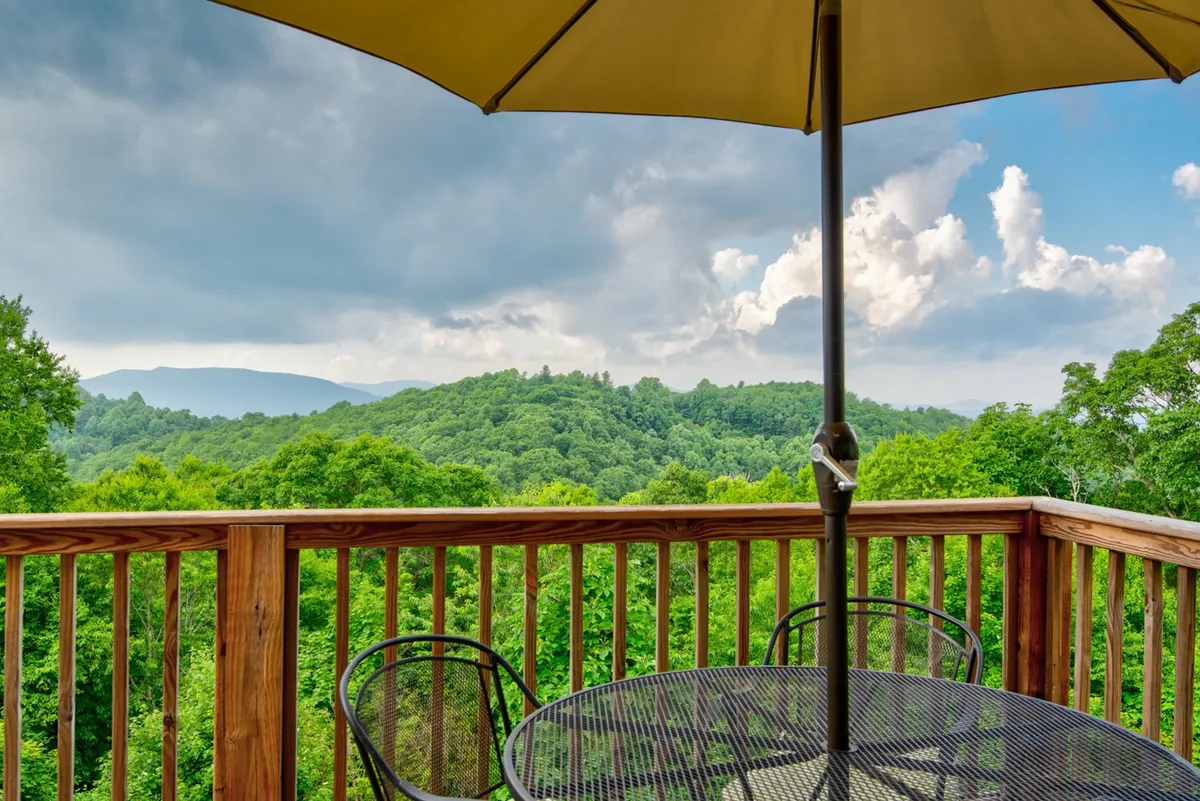 An outdoor dining table and chairs with an umbrella set on the deck, overlooking a sweeping mountainous view. The scene is serene and invites guests to relax, enjoy meals, and take in the stunning landscape. The table setup hints at leisurely mornings or twilight gatherings.