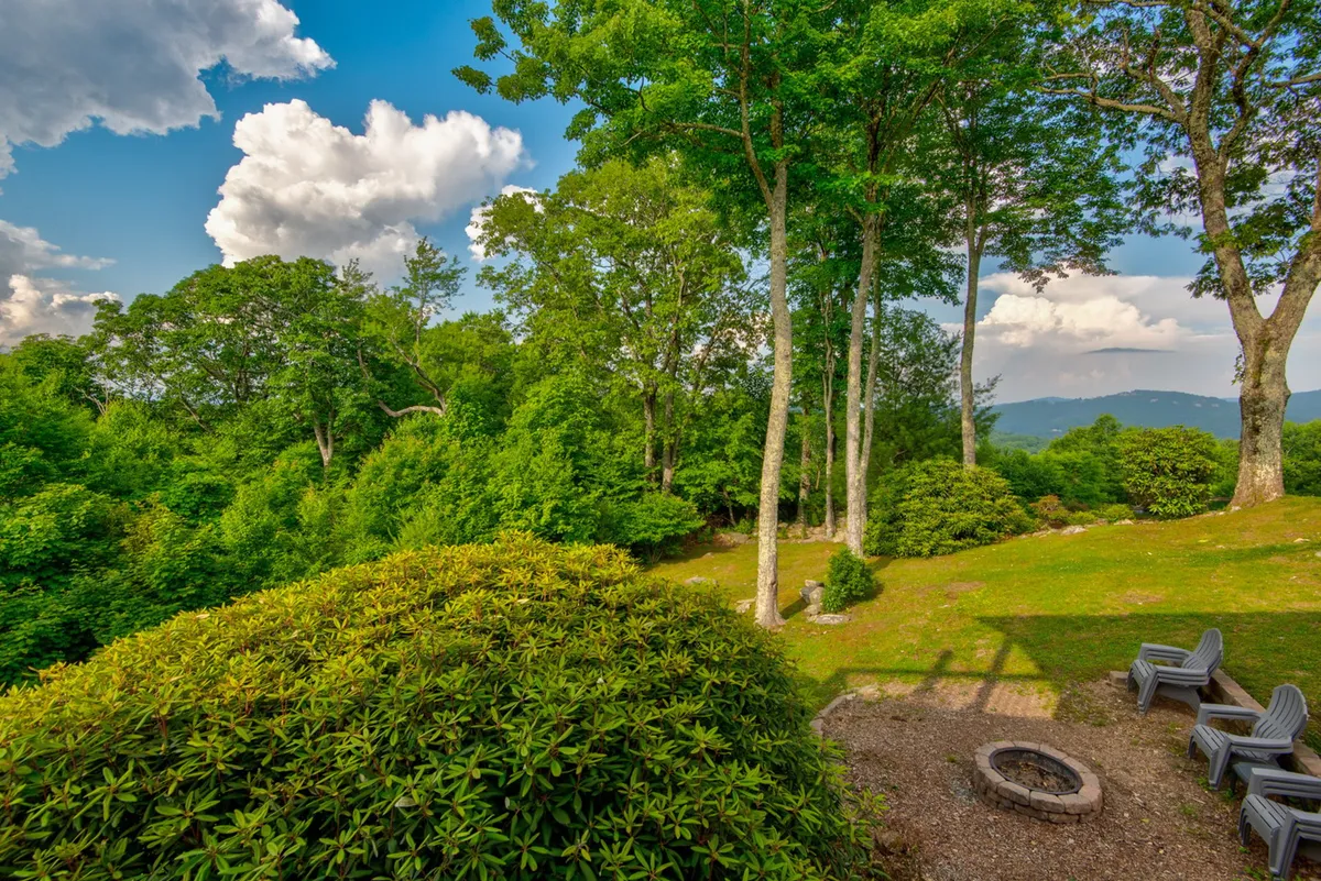 A cozy outdoor fire pit area with lounge chairs set amidst lush greenery, looking out toward distant mountains. The space is ideal for gathering at sunset or enjoying star-filled nights with friends and family.